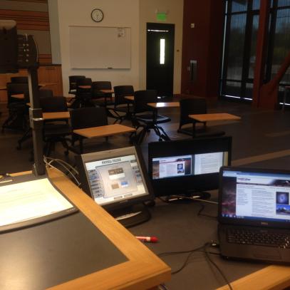 Classroom in background lectern in foreground with laptop, document camera, touch panel and monitor