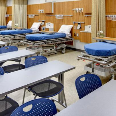 Row of tables in middle of room with a 6 hopsital bed bays on wall